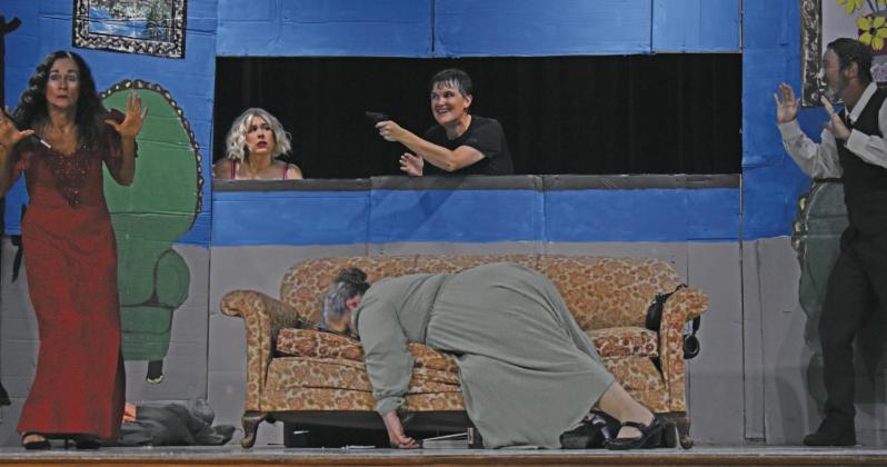 Chevy Carter (center window) holds up the cast of the play within the play in “Drop Dead!”. Left standing is Tawny K Duren and far right standing is David Timmons. DaNae Peters stands next to Carter, while Dani Skelton plays dead on the couch. Photo/Emily Kalka