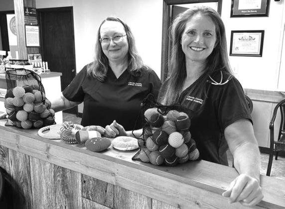 On the left, Jayne Bell and Dr. Theresa McKinzie pose with pet toys donated by Harrah’s Oklahoma at the Lincoln County Animal Hospital. On the right, Librarian Sandy Tharp-Thee sits with books that were donated by the casino. Photos/Harrah’s Oklahoma