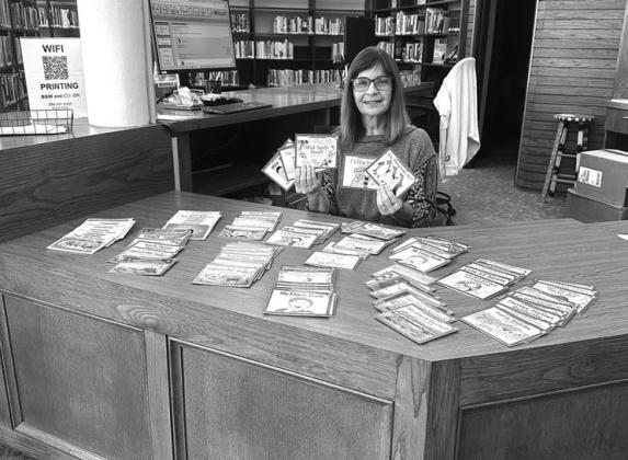 On the left, Jayne Bell and Dr. Theresa McKinzie pose with pet toys donated by Harrah’s Oklahoma at the Lincoln County Animal Hospital. On the right, Librarian Sandy Tharp-Thee sits with books that were donated by the casino. Photos/Harrah’s Oklahoma