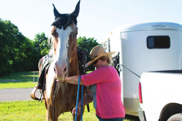 Pictured above to the right, Jim Shingleton hugs Veva Jiles as they stand in between Kid to their left and Gus to their right. Pictured below, Alana Owen takes the reigns off her horse, King, after a long trail ride. Photos/Chelsea Weeks.