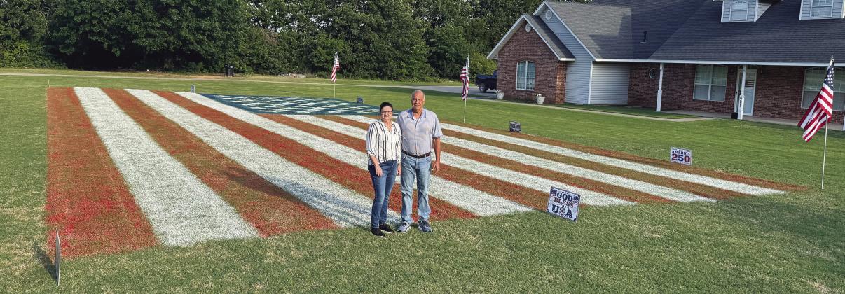 Janet and Gary Hodde stand in front of the giant U.S. flag that they painted in their front yard in McLoud. It took nearly two days and 85 gallons of paint to complete the project. Photo/Brian Blansett