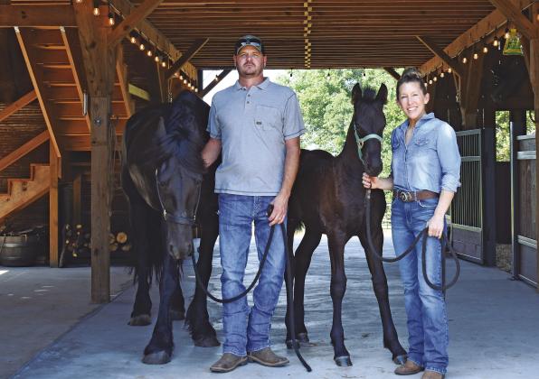 McLoud couple Cory (left) and Melody (right) Martin stand inside their stable with their two Fresians, Lady Lorelei (left) and her daughter, Aurora Avail (left). The two built the stable themselves with help from friends and family. Melody is passionate about sharing her love for Fresian horses, as well as the many causes she champions and supports, such as Cargo Ranch and Guardians of the Forest. Photo/Emily Kalka