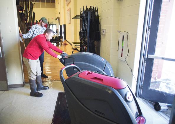 North Rock Creek athletic director Evan Smith (red shirt) and middle school principal Justin MacDonald try to clear water from the school gym’s Saturday morning. The school had to relocate regional tournaments that were scheduled there this week because the water buckled the gym floor. Photo/Brian Blansett