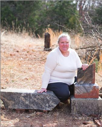 Pictured to the right, Cheryl Johnson sits by the grave of her great great grandfather, Lars Johnson. Photo/Chelsea Weeks