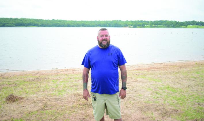 Stroud Lake Ranger Jared Null stands on the shore of the lake in the swimming area on May 29. The lake recently added self-serve kayak rentals and a new 18-hole disc golf course. Null said the lake has grants to build a new dock, improve equestrian trails and build a new playground in the near future. Photo/Emily Kalka