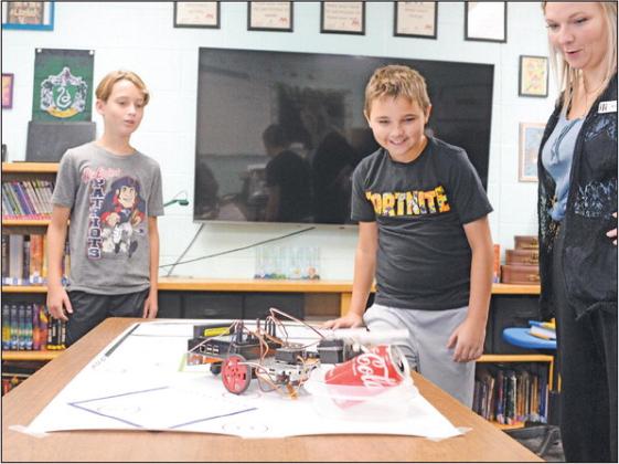 Tyson Pittman, left, and Logan Hand watch with Wellston Gifted and Talented teacher Nicole Reeves as their robot completes its task of locating a Coca-Cola can, grasping it and depositing it in a container. Photo/Brian Blansett