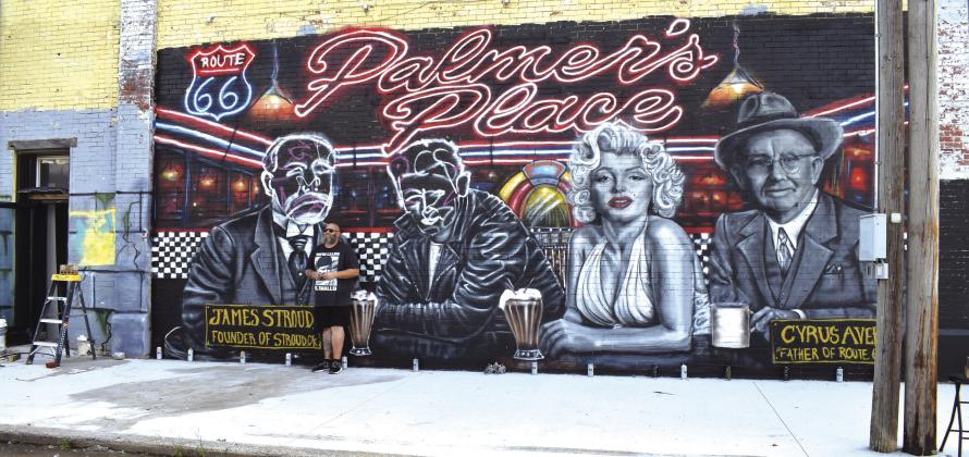 Artist Collin Birchmier stands in front of his almost-finished mural on the side of Palmer’s Place on Main Street in Stroud. Photo/Emily Kalka