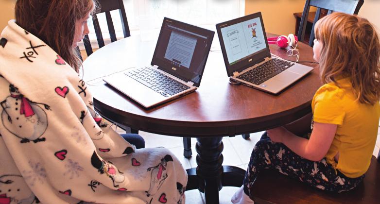 Sisters Aaliyah, left, and Melody Coffman work online assignments at the kitchen table on the first day of at-home school Monday. Photo/Brian Blansett