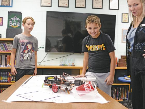 Tyson Pittman, left, and Logan Hand watch with Wellston Gifted and Talented teacher Nicole Reeves as their robot completes its task of locating a Coca-Cola can, grasping it and depositing it in a container. Photo/Brian Blansett