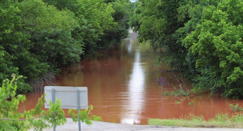 County Road 940 just north of the Deep Fork River was a couple of feet deep Sunday morning. The sign at right reads: “No parking any time.” Photo/Brian Blansett