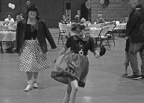 Jennifer Alsip (left) follows her daughter Joy Alsip (right) as they make their way through the stroll at the Route 66 100th Birthday party on Friday. The evening had dancing, a soda shop, concession stand, costume contest and a dance contest. Photo/Emily Kalka