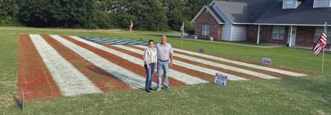 Janet and Gary Hodde stand in front of the giant U.S. flag that they painted in their front yard in McLoud. It took nearly two days and 85 gallons of paint to complete the project. Photo/Brian Blansett