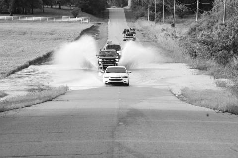 Cars and trucks splash through flooded Econtuchka Road north of the North Canadian River in Pott County. The nearby bridge and road were