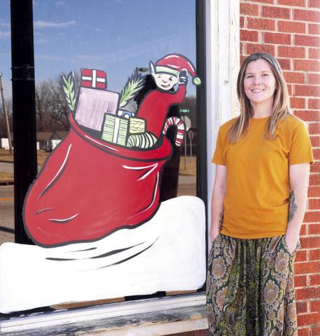 Courtney Lyon is pictured with one of the many windows in Stroud she painted to go along with the Illuminated Elf Christmas theme. This is her second year to do this. Photo/Baylee Billings