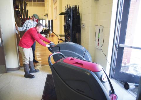 North Rock Creek athletic director Evan Smith (red shirt) and middle school principal Justin MacDonald try to clear water from the school gym’s Saturday morning. The school had to relocate regional tournaments that were scheduled there this week because the water buckled the gym floor. Photo/Brian Blansett