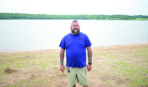 Stroud Lake Ranger Jared Null stands on the shore of the lake in the swimming area on May 29. The lake recently added self-serve kayak rentals and a new 18-hole disc golf course. Null said the lake has grants to build a new dock, improve equestrian trails and build a new playground in the near future. Photo/Emily Kalka