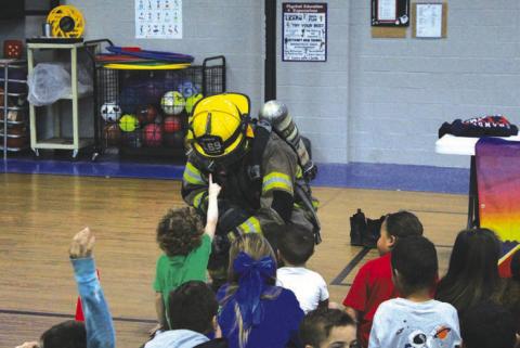 The Chandler Fire Department spent time at East Side Elementary teaching kids about fire safety last week. In the photo on left, Ben Froh shows off his gear to a curious child. On the right, Asst. Fire Chief Tony Rednour explaining what a halligan bar is and how it works. Photos/Landon Gray