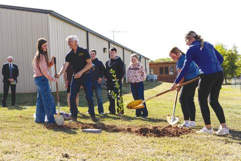 From left to right, Josie Murray, Wylee Terrell, Tate McConnell, Hayden Green, Rowan Shelton, Kirbey McConnell and Savanah Gaylord help a representative from the Oklahoma Forestry Service plant a memorial sapling at Wellston High School.